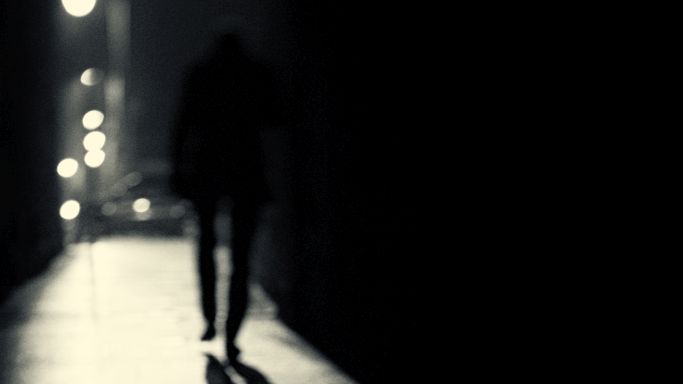 Das Bild zeigt die Silhouette der Rückseite einer Person bei Nacht, die allein eine Unterführung entlang schreitet